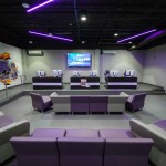 Empty NSU Esports venue with couches and chairs in the foreground and PCs in the background. A mural is on the left wall.