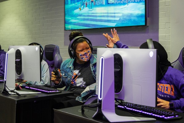 Two female students high-five each other while sitting at desktop PCs.