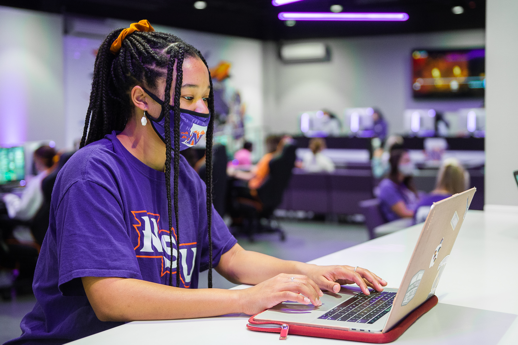 A masked female student sits typing at her laptop in the NSU Esports Venue.