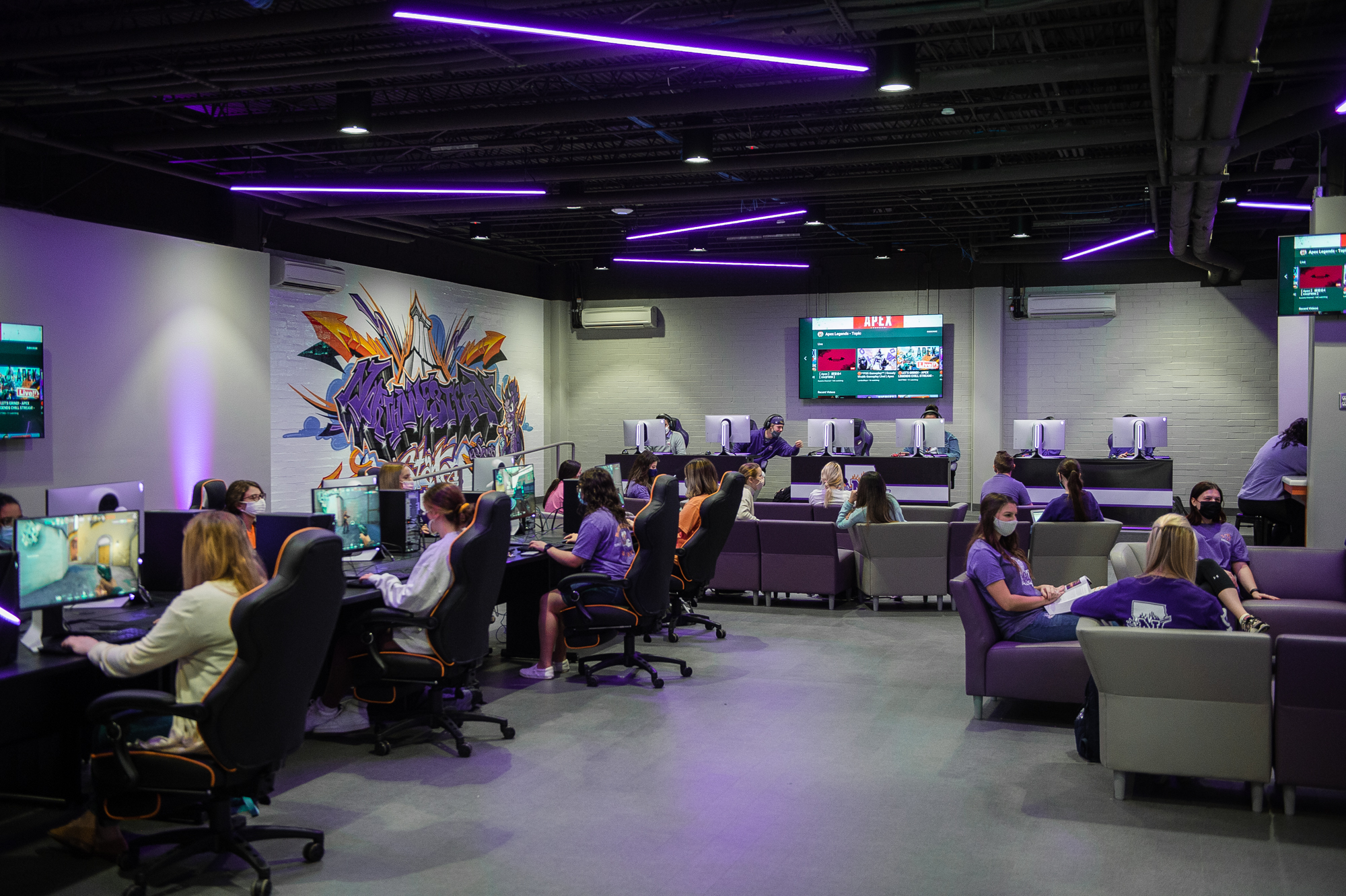 In the NSU Esports Venue, some students game at desktop PCs while others relax and chat with each other on the lounge furniture.