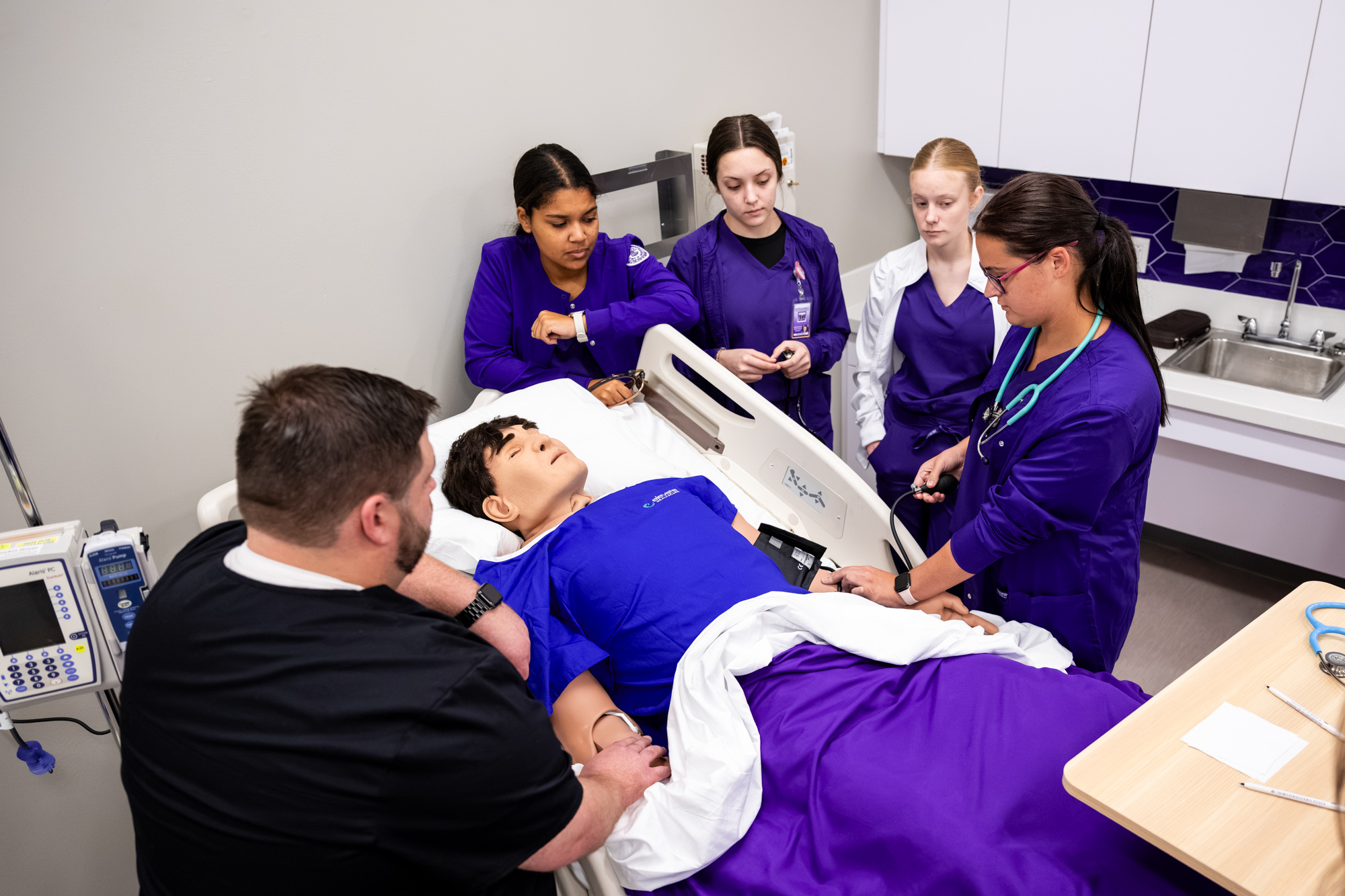 nursing students and faculty standing around a hospital bed