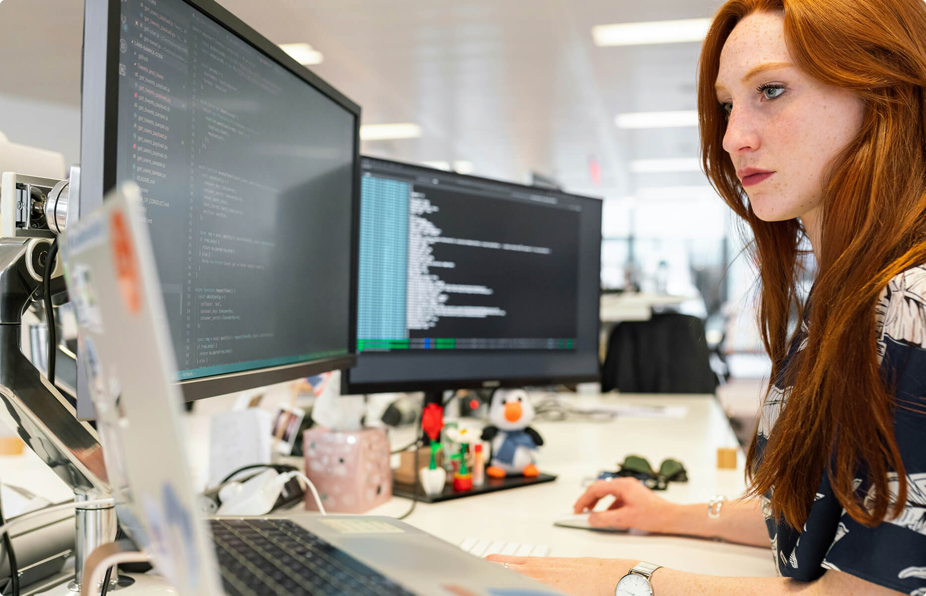 A woman working at two computer monitors and a laptop.