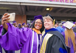 A student and faculty member wearing graduation caps and gowns.
