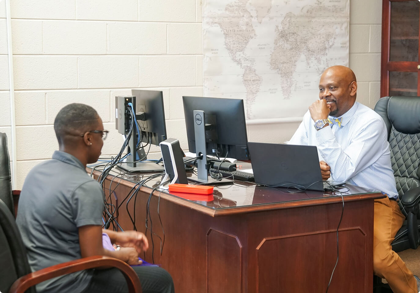 Two people sitting around a desk with a computer.