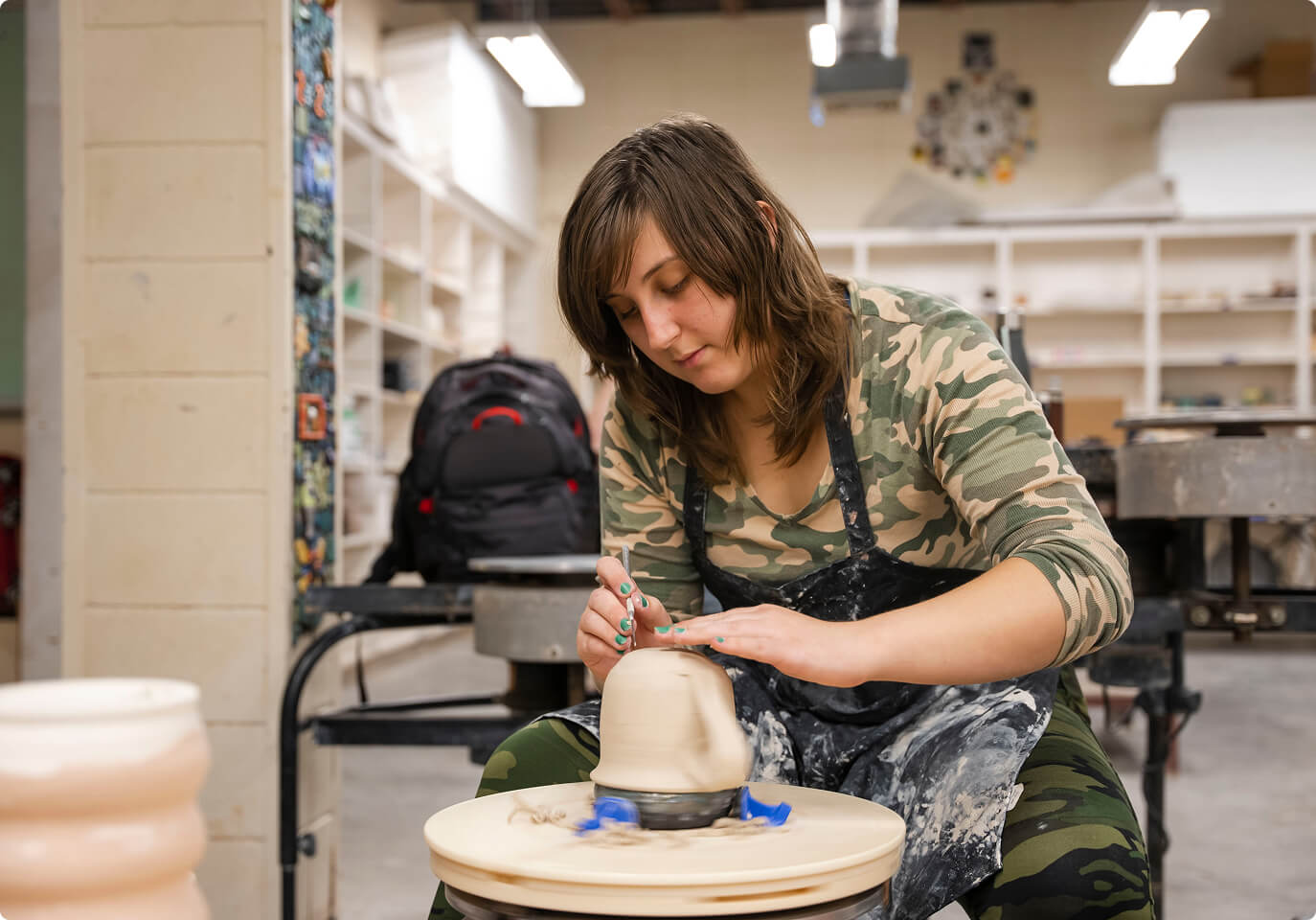 A student sculpting clay on a wheel.