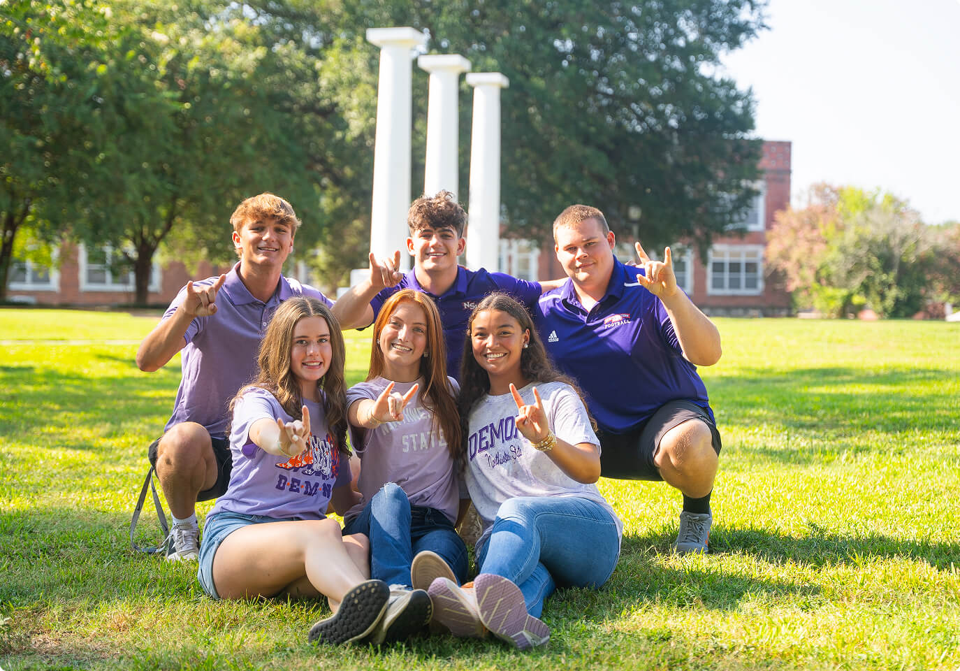 Several students posing on a grassy field with the demon hand symbol.
