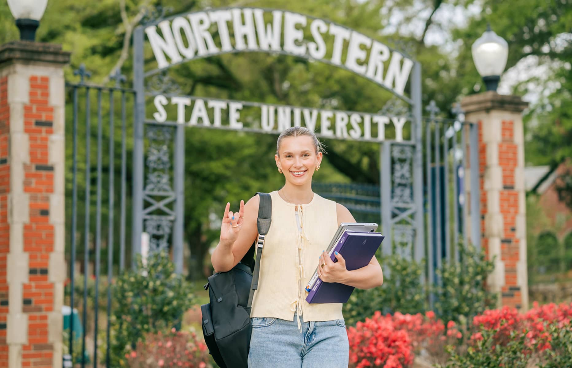 Student holding textbooks in front of of gated entrance