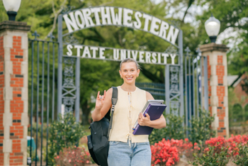 NSU student poses at the entrance of campus with their laptop and books