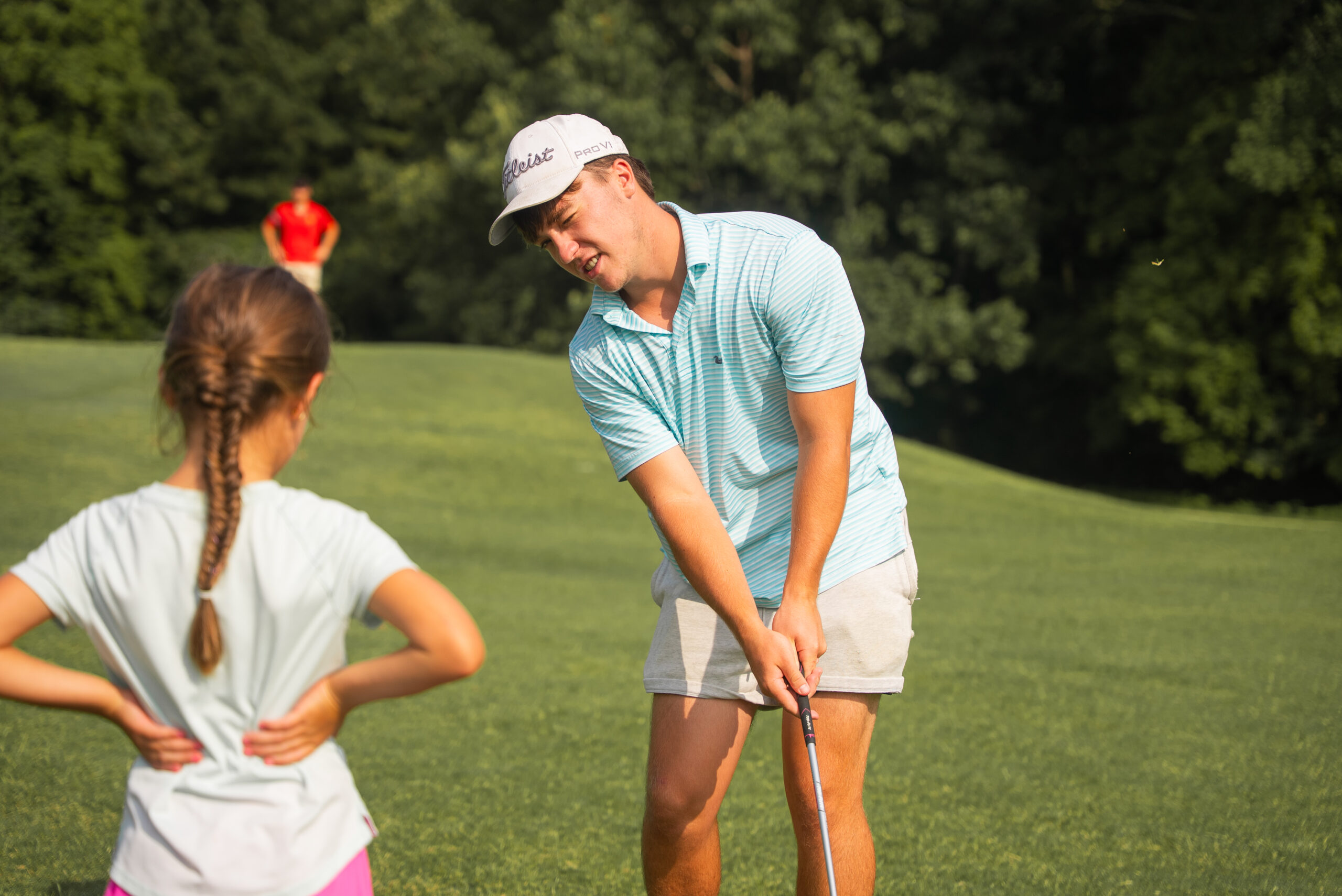 An NSU student demonstrates a golf swing for a young camper