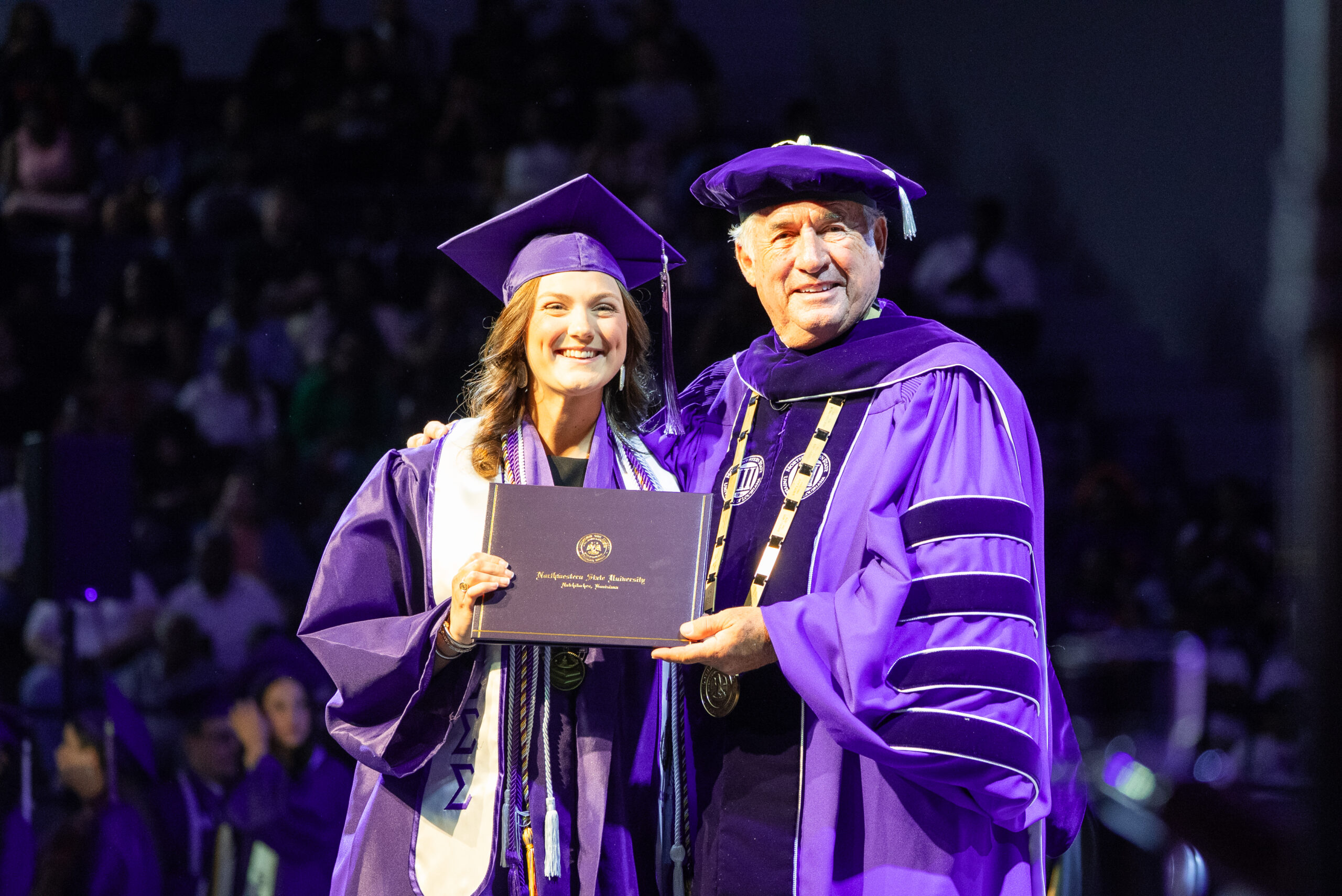 NSU graduate poses for a photo on stage with President Genovese