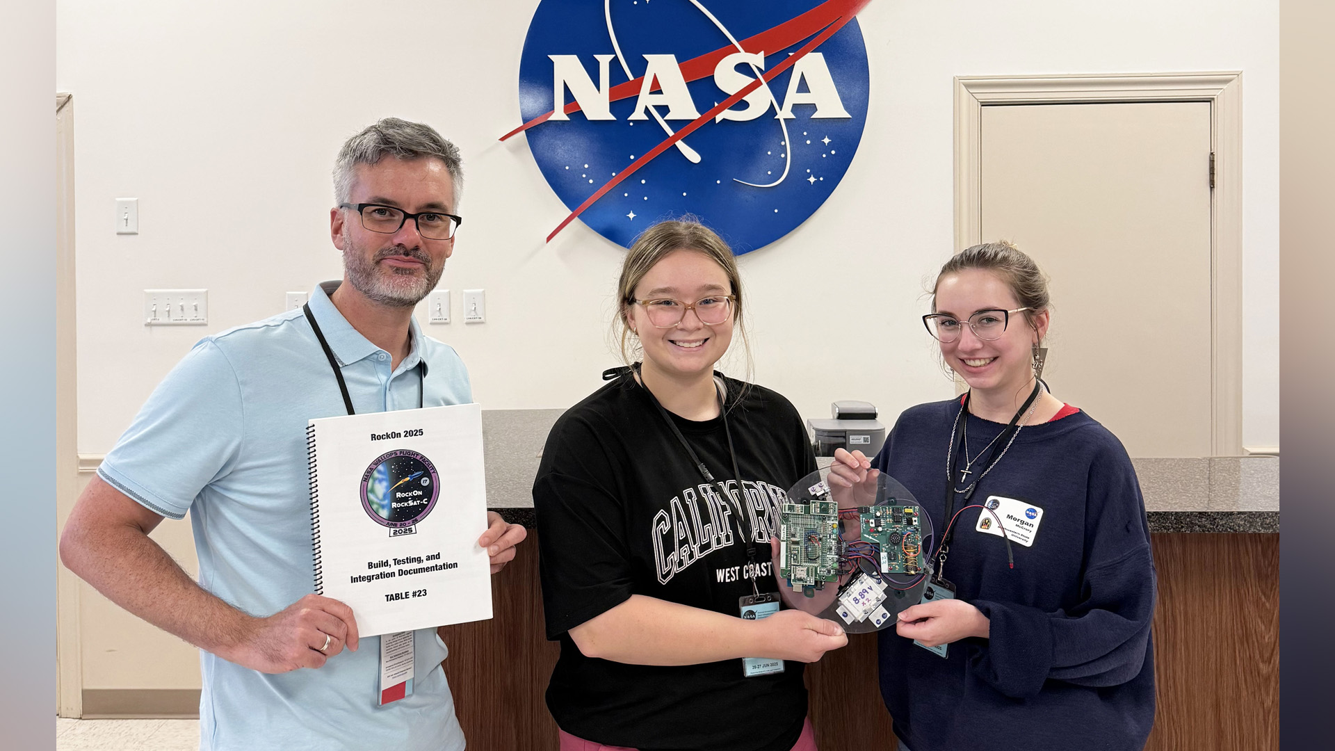 Dr. Damien Tristant, Shae Wetzel and Morgan McCrory, from left, are shown during the 2025 RockOn program at NASA’s Wallops Flight Facility on Wallops Island, Virginia, holding the checklist manual and their assembled payload after completing the soldering and coding stages.