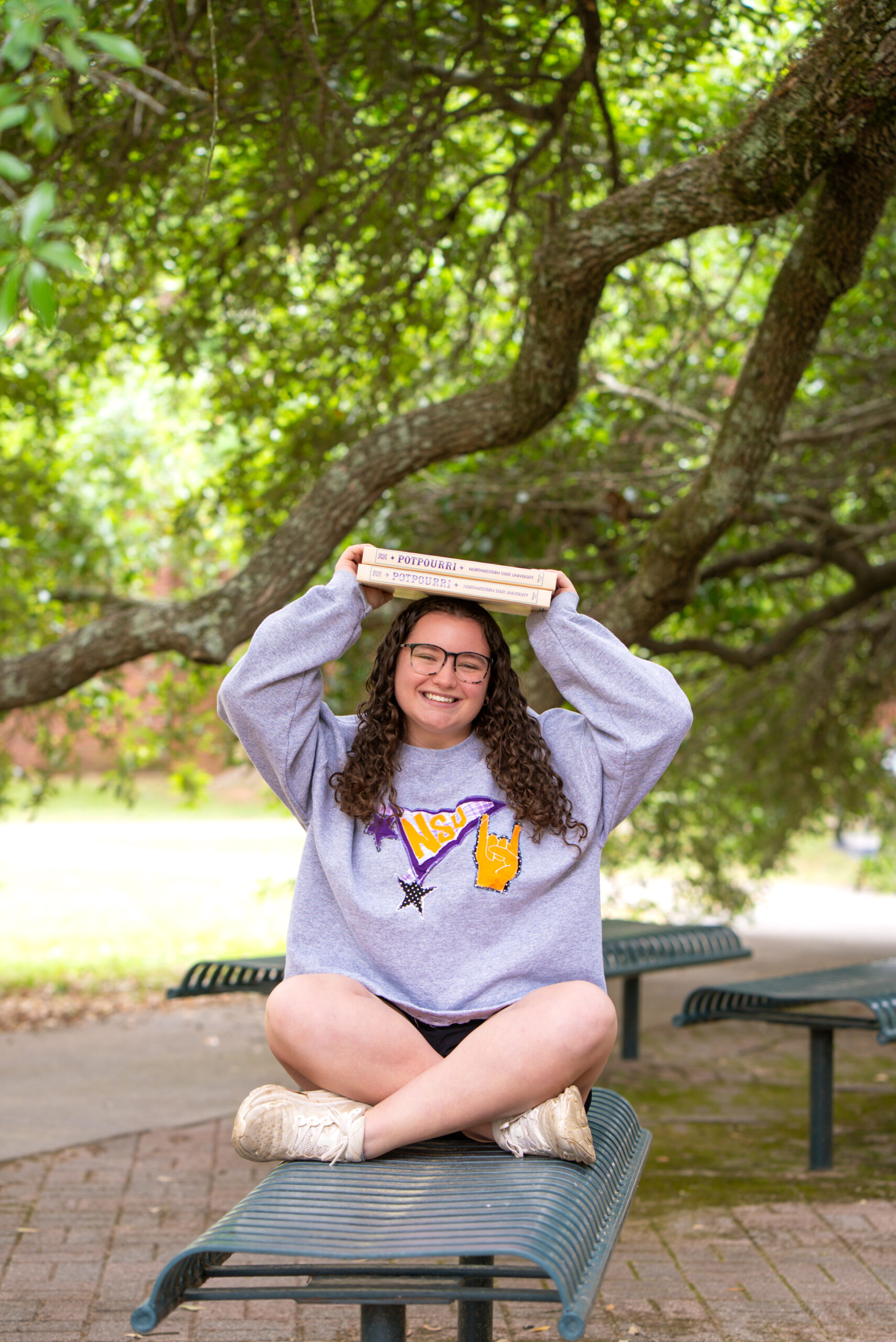 NSU student sitting on a bench with two yearbooks on her head