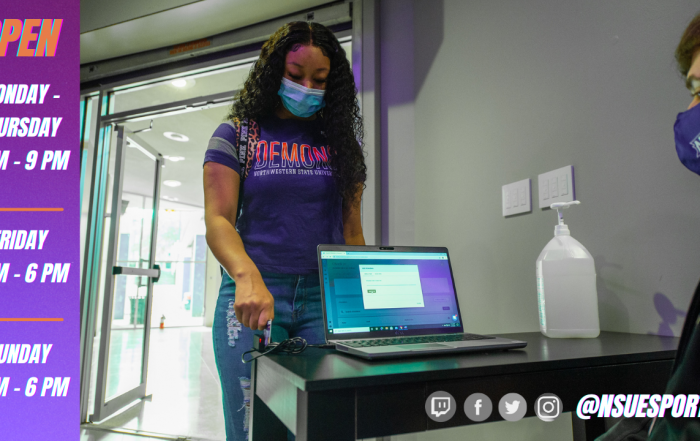 A masked female student swipes her ID at the NSU Esports check-in desk attended by a masked male student.