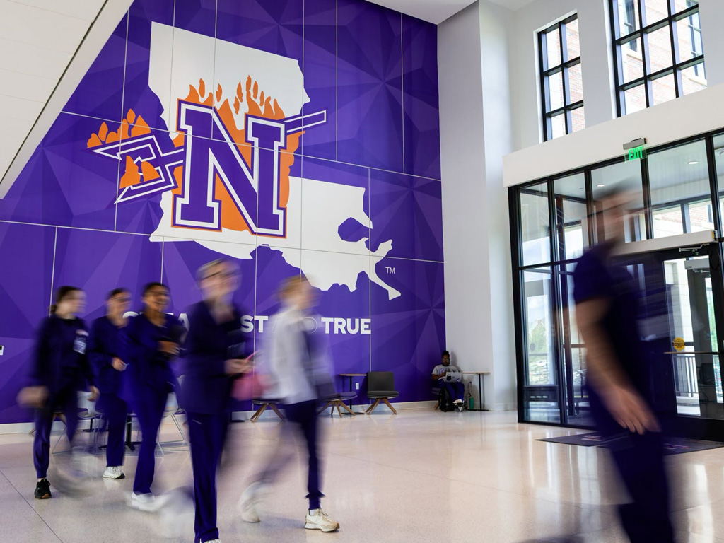 Students walking through a bright hallway featuring a large wall graphic of Northwestern State University of Louisiana.